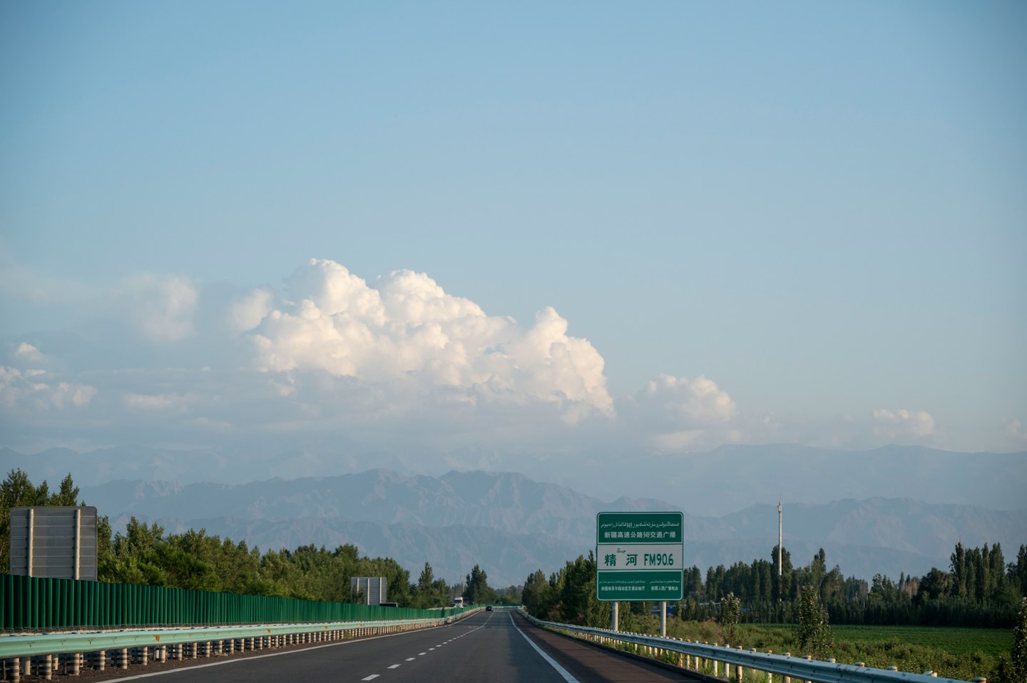 Coches circulan por una autopista rodeada de árboles verdes y montañas.