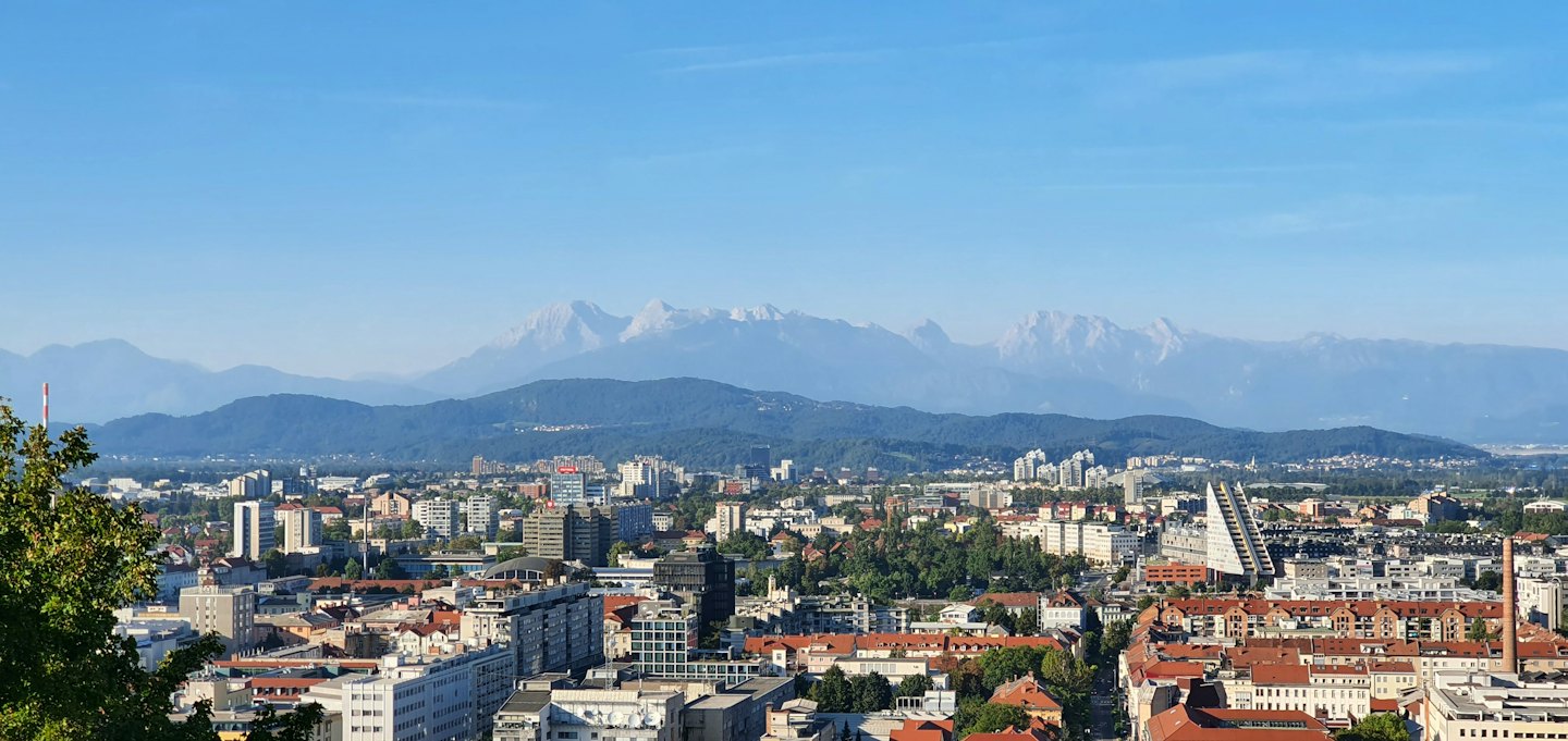 Edificios de la ciudad y colinas boscosas se alzan ante montañas nevadas.